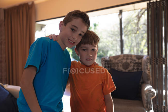 Retrato de dos niños caucásicos preadolescentes en la sala de estar en casa mirando a la cámara - foto de stock