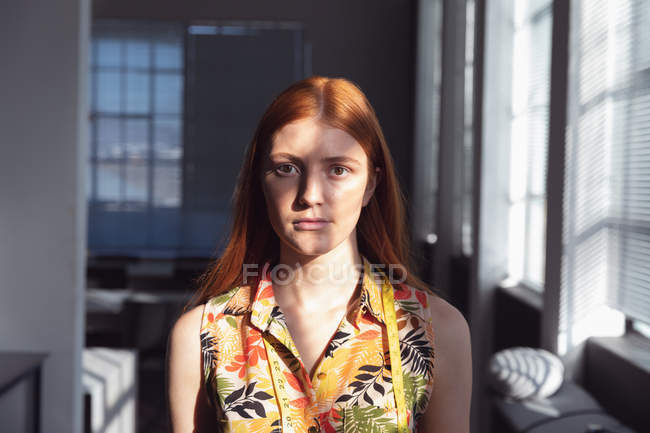 Retrato de perto de uma jovem estudante de moda caucasiana olhando diretamente para a câmera por uma janela, com luz solar e sombra em seu rosto — Fotografia de Stock