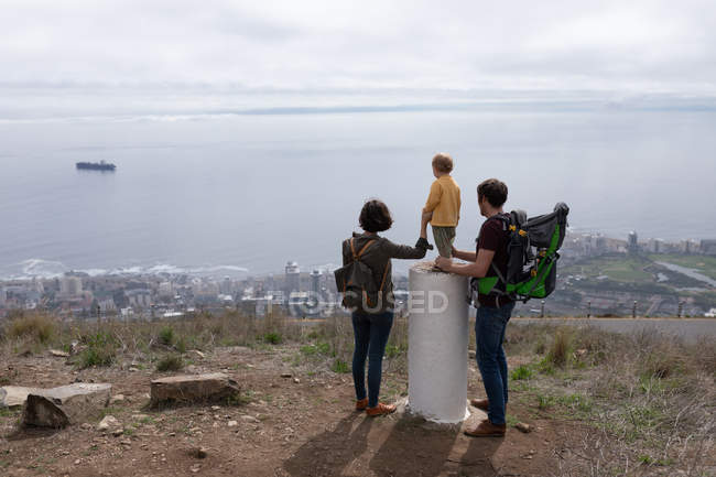 Rear view of a young Caucasian father and mother standing in a park with their baby between them and enjoying the view — Stock Photo