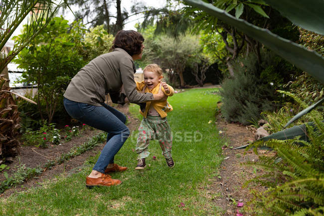 Vista laterale di una giovane madre caucasica che prende il suo bambino in un giardino — Foto stock