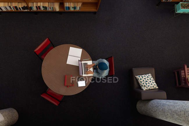 Overhead-Ansicht einer jungen asiatischen Studentin mit Turban, die einen Laptop benutzt und in einer Bibliothek studiert — Stockfoto