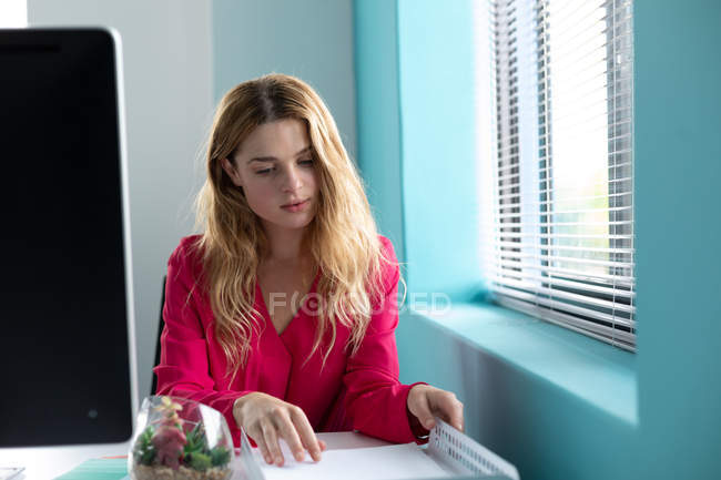 Nahaufnahme einer jungen kaukasischen Frau, die an einem Schreibtisch sitzt und in einem Tablett im modernen Büro eines Kreativunternehmens Papierkram betrachtet — Stockfoto