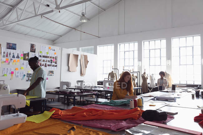 Front view of a young African American male, a young Caucasian and a young mixed race female fashion students all working on their designs in a studio at fashion college — Stock Photo
