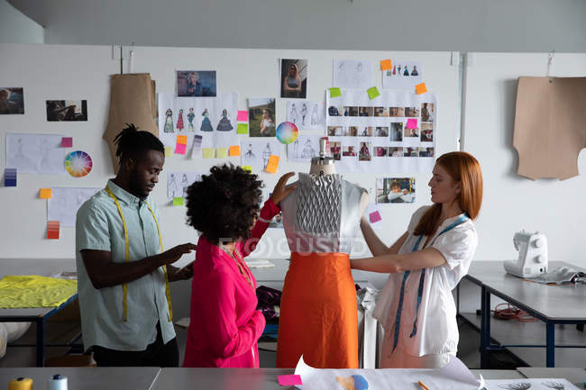Vista lateral de um jovem afro-americano, uma mulher caucasiana e uma mista estudantes de moda feminina trabalhando no design de roupas em um manequim em um estúdio na faculdade de moda — Fotografia de Stock