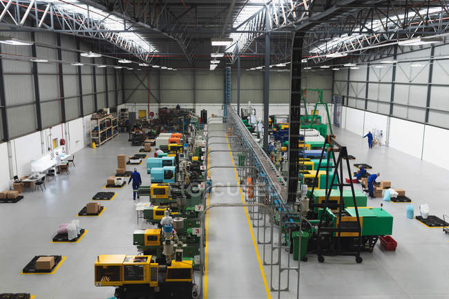 High angle view of two rows of processing equipment and the packing area in a warehouse at a processing plant, with factory workers visible working in the background — Stock Photo