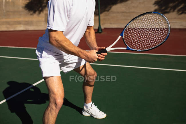 Вид збоку крупним планом чоловік грає в теніс в сонячний день, тримає ракетку і чекає м'яча — стокове фото