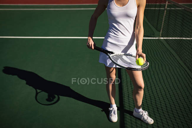 Передній вид жінки, яка грає в теніс в сонячний день, стоїть біля сітки і тримає ракетку і м'яч — стокове фото