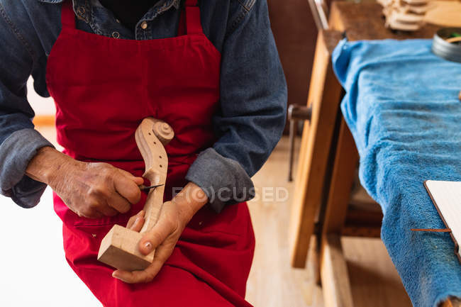 Nahaufnahme einer Geigenbauerin bei der Arbeit an der Rolle einer Geige in ihrer Werkstatt mit einer Werkbank neben ihr — Stockfoto