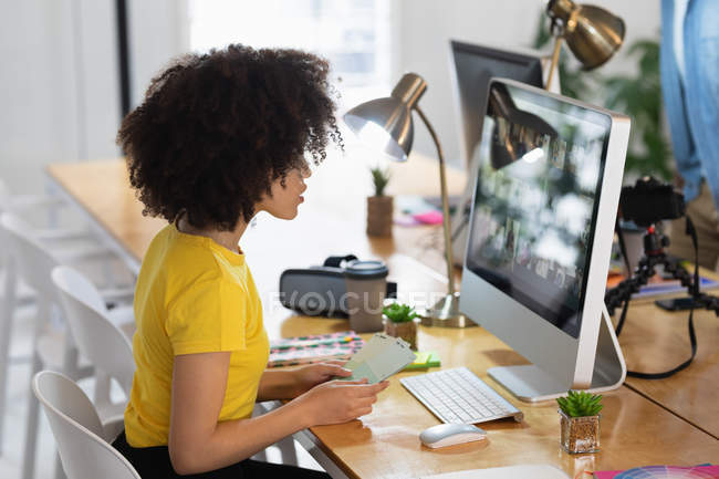 Вид збоку крупним планом молода змішана жінка, що сидить за столом і дивиться на екран комп'ютера в творчому офісі — стокове фото