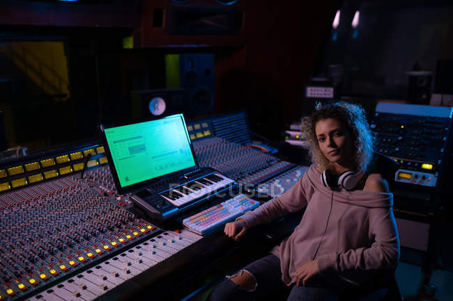 Portrait of a young Caucasian female sound engineer sitting at a mixing desk in a recording studio looking to camera — Stock Photo