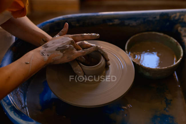 Gros plan élevé des mains d'une potière façonnant de l'argile humide dans un pot sur une roue de potiers dans un atelier de poterie — Photo de stock