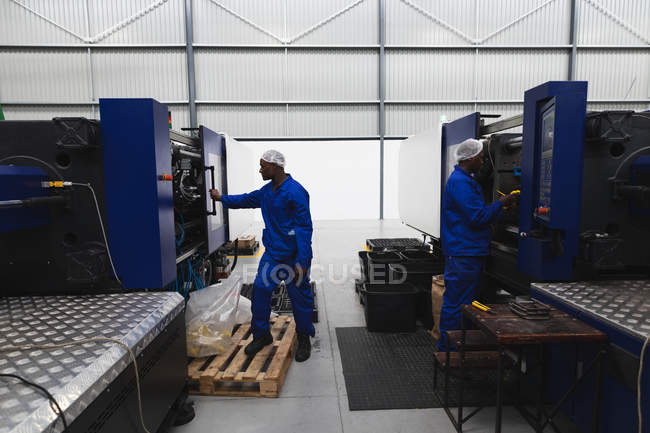 Seitenansicht von zwei jungen afrikanisch-amerikanischen männlichen Fabrikarbeitern, die Geräte in einer Fabrikverarbeitungsanlage bedienen — Stockfoto