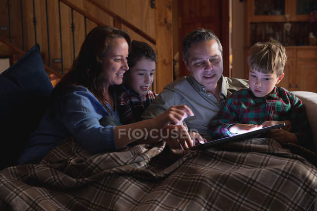 Vue de face gros plan d'un homme et d'une femme caucasiens d'âge moyen utilisant une tablette avec leurs deux fils pré-adolescents à la maison — Photo de stock