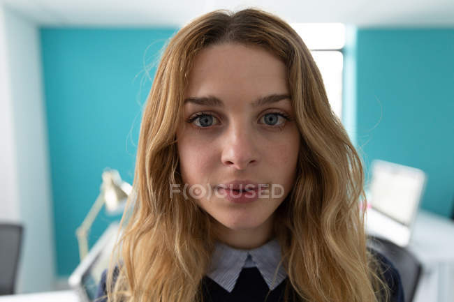 Portrait close up of a young Caucasian woman with long blonde hair and blue eyes looking straight to camera in the office of a creative business — Stock Photo
