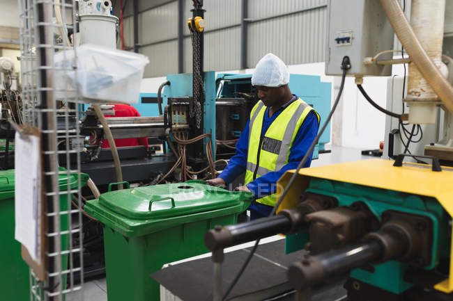 Вид сбоку. Молодой афроамериканец, работающий на фабрике, перевозит грин на складе на перерабатывающем заводе в окружении оборудования и оборудования. — стоковое фото