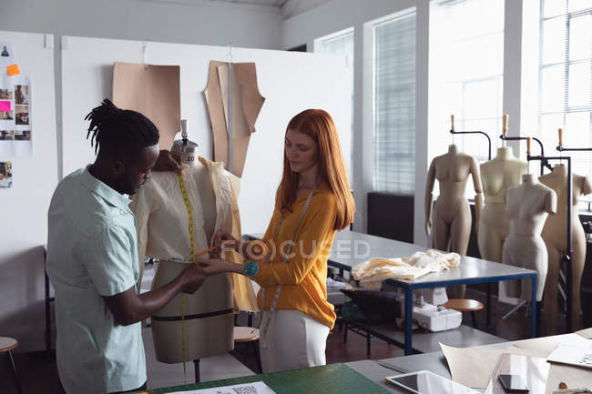 Вид спереди на молодого афроамериканского мужчину и молодую кавказскую студентку моды, работающую над дизайном манекена в студии колледжа моды — стоковое фото