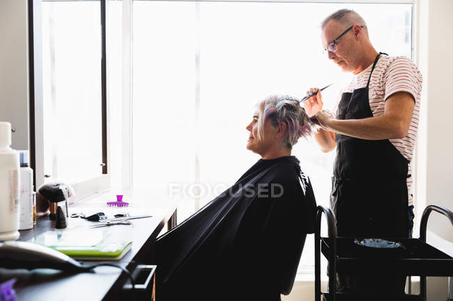 Side view of a middle aged Caucasian male hairdresser and a young Caucasian woman having her hair colored in a hair salon — Stock Photo