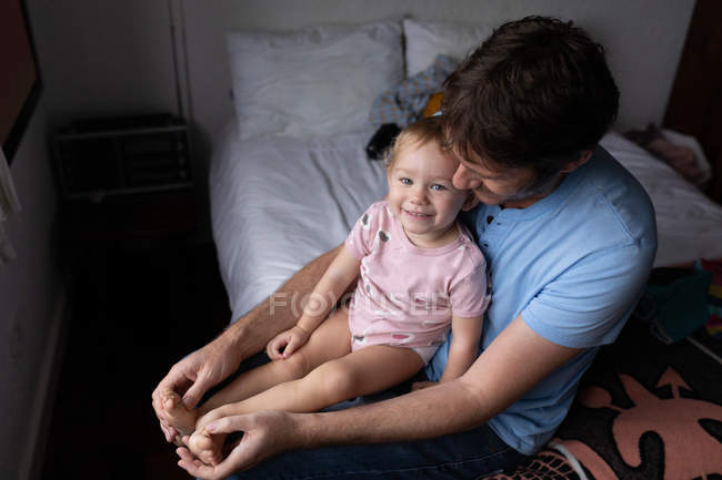 Перед очима молодого кавказького батька, який тримає усміхнене дитя, сидячи на ліжку. — стокове фото