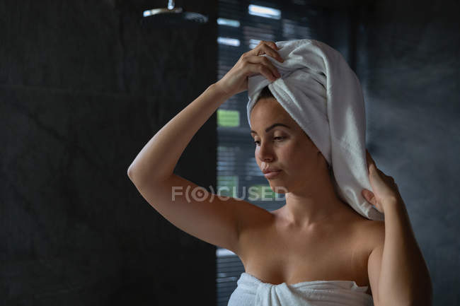 Vista frontal close-up de uma jovem mulher morena caucasiana vestindo uma toalha de banho envolvendo seu cabelo em uma toalha, em um banheiro moderno — Fotografia de Stock