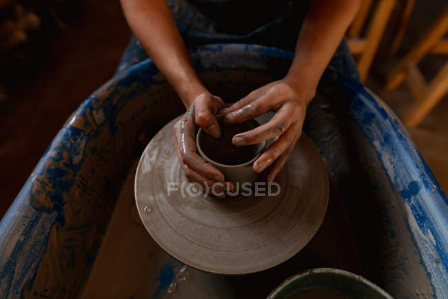 Elevated close up of the hands of female potter shaping wet clay into a pot shape on a potters wheel in a pottery studio — Stock Photo