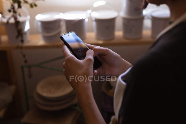 Vista laterale sezione centrale del vasaio femminile utilizzando uno smartphone in uno studio di ceramica — Foto stock