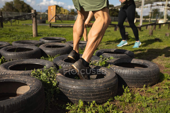 Unterschnitt eines Mannes, der während eines Bootcamp-Trainings in einem Outdoor-Fitnessstudio durch Reifen tritt — Stockfoto