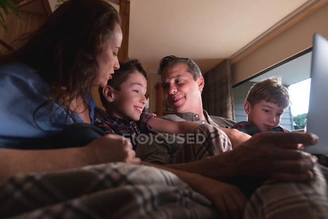 Вид спереди: мужчина и женщина средних лет с двумя сыновьями-подростками, сидящими дома за ноутбуком — стоковое фото