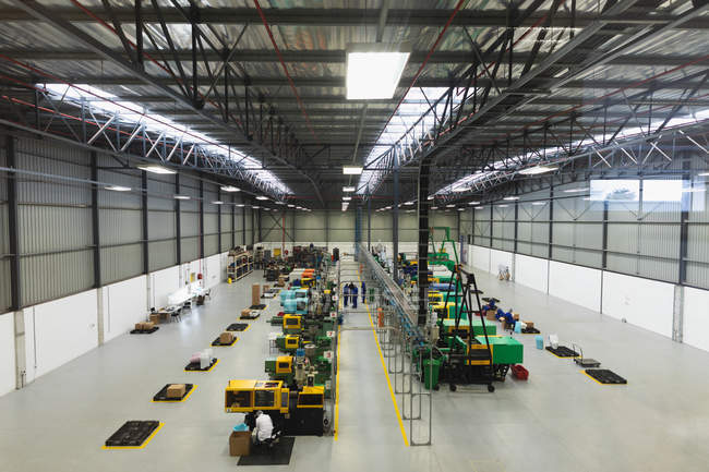 Hochwinkelaufnahme von Fabrikarbeitern, die Maschinen bedienen und in einem Lager in einem Fabrikverarbeitungsbetrieb interagieren — Stockfoto