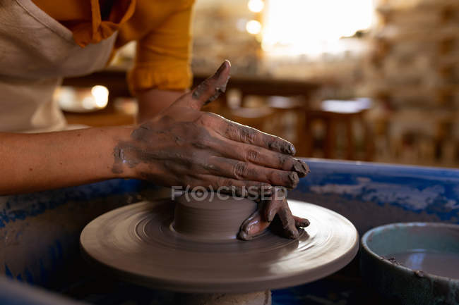 Close up of the hands of female potter shaping wet clay on a potters wheel in a pottery studio — Stock Photo