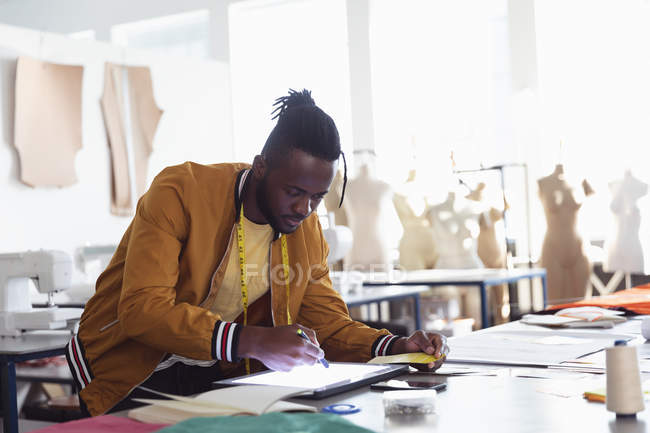 Vista laterale di un giovane studente afroamericano di moda maschile che lavora su un design utilizzando un tablet e uno stilo in uno studio al college di moda — Foto stock