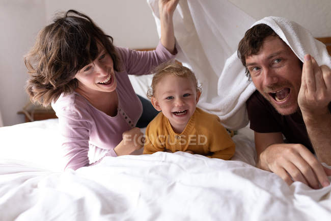 Портрет молодого кавказького батька і матері, які лежать на ліжку з дитиною посміхаючись до камери — стокове фото