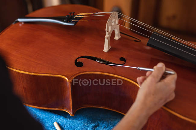 Close up of female luthier working on the body of a cello on a workbench in her workshop — Stock Photo