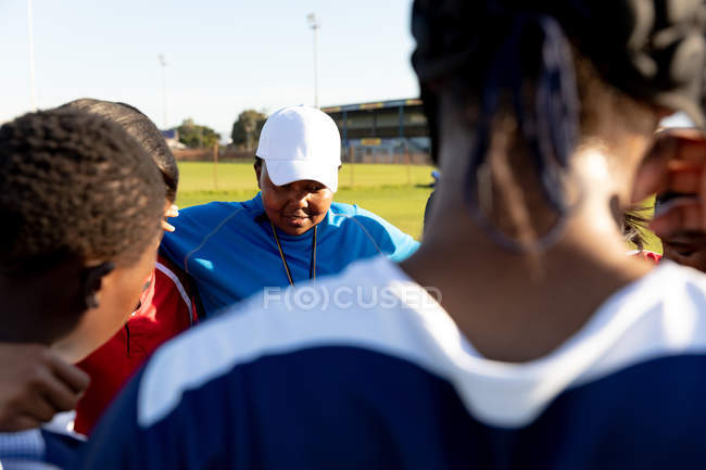 Over the shoulder view of a team of young adult multi-ethnic female rugby players and their middle aged mixed race female coach standing in a huddle on a rugby field preparing for a rugby match — Stock Photo