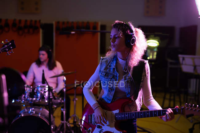 Front view of a young Caucasian female singer guitarist playing an electric guitar and a young Caucasian male drummer performing during a session at a recording studio — Stock Photo
