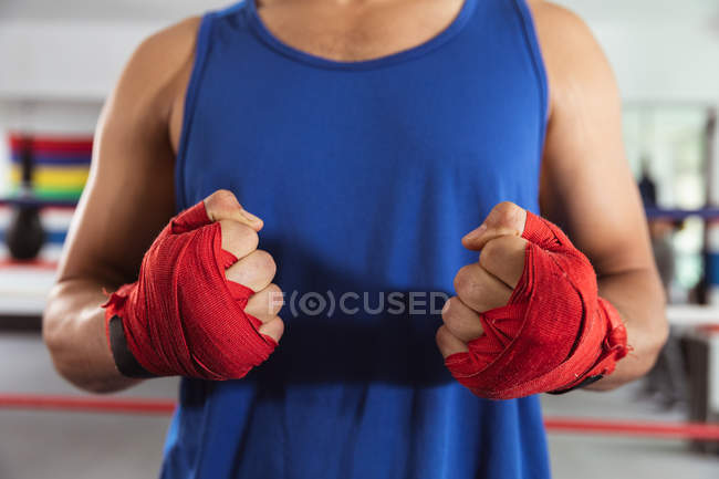 Vista frontal sección media del boxeador masculino en un anillo de boxeo con las manos envueltas - foto de stock
