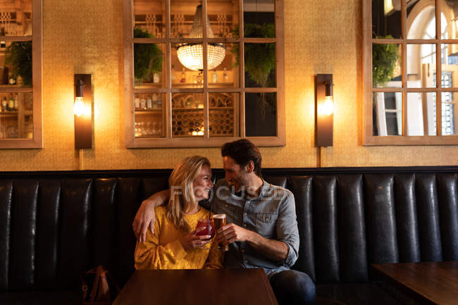 Вид на щаслива молода кавказька пара відпочиваючи разом у відпустку в барі, обіймаючи, питне пиво і коктейль — стокове фото