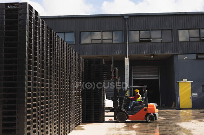 Vista laterale di un operaio caucasico di mezza età che utilizza un carrello elevatore per spostare una pila di pallet fuori da un magazzino in una fabbrica — Foto stock