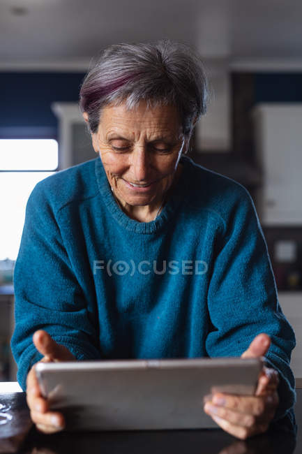 Вид спереду крупним планом старший кавказька жінка на кухні за допомогою планшетного комп'ютера — стокове фото