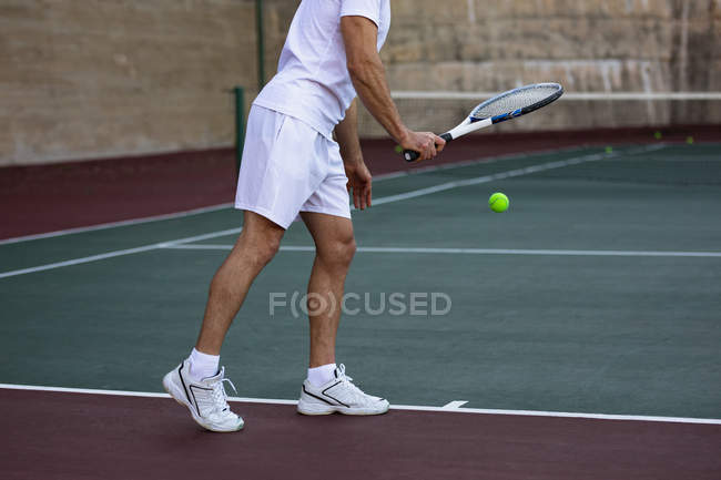Seitenansicht eines Mannes, der Tennis spielt und sich darauf vorbereitet, mit einer Wand im Hintergrund zu dienen — Stockfoto