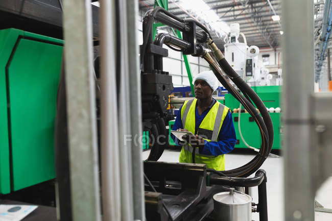 Передній вигляд молодого афроамериканського робітника на фабриці, який тримає дошку для пасажирів і перевіряє обладнання на фабриці. — стокове фото