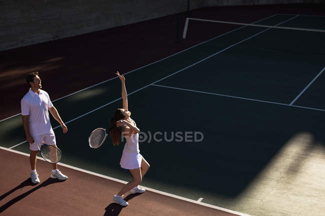 Vista lateral de una joven mujer caucásica y un hombre jugando tenis en un día soleado, sirviendo mujer - foto de stock