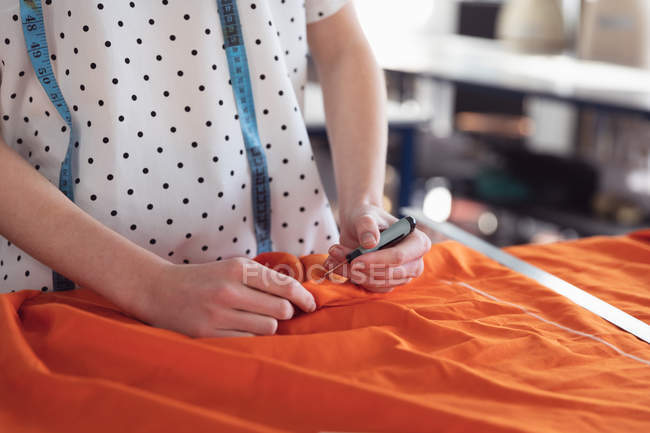 Visão frontal seção média de estudante de moda feminina trabalhando em um design com tecido laranja em um estúdio na faculdade de moda — Fotografia de Stock