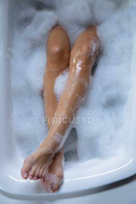 Cierra las piernas de una mujer, levantada en el borde mientras se acuesta en un baño de espuma - foto de stock
