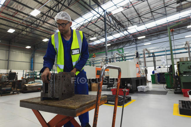 Front view close up of a middle aged mixed race male factory worker wearing glasses and workwear preparing a machine part in a warehouse at a processing plant — Stock Photo