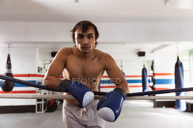Retrato de un joven boxeador mestizo apoyado en una cuerda de un anillo de boxeo - foto de stock