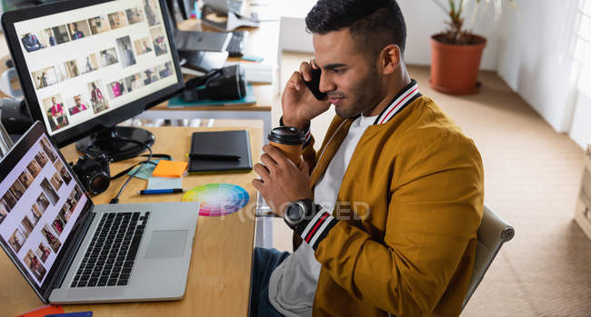 Вид збоку крупним планом молодий змішаний чоловік, що сидить за столом і використовує смартфон у творчому офісі — стокове фото
