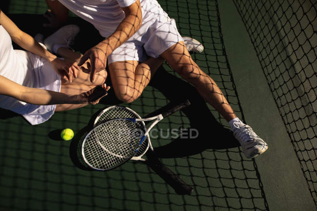 Frontansicht einer Frau und eines Mannes, die an einem sonnigen Tag auf einem Tennisplatz sitzen und ein Selfie machen — Stockfoto