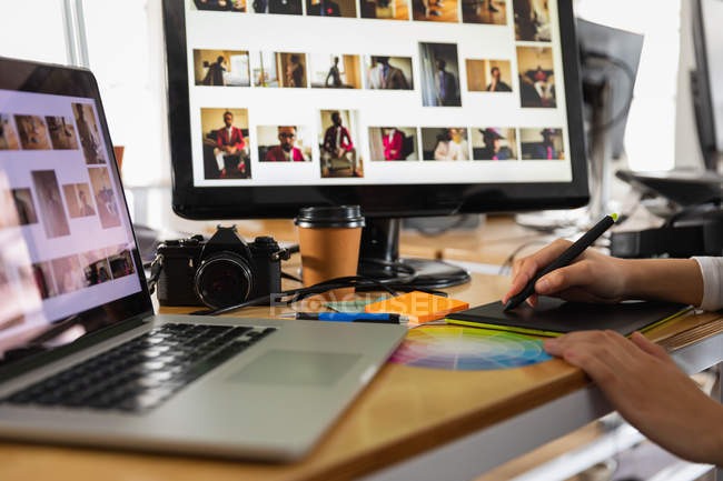Close-up de mãos de uma mulher sentada em uma mesa com um computador portátil, uma tela de computador usando uma caneta e um tablet gráfico em um escritório criativo — Fotografia de Stock