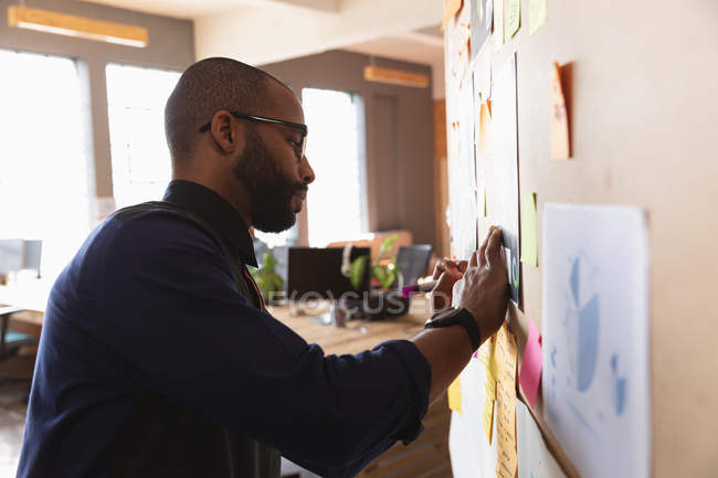 Vista laterale da vicino di un giovane afroamericano che scrive appunti su un muro durante una sessione di brainstorming di squadra in un ufficio creativo — Foto stock