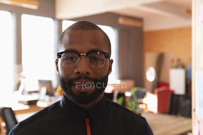 Portrait close up of a young African American man with short hair, a beard  and wearing glasses looking to camera in a creative office — work, cool -  Stock Photo | #307087266